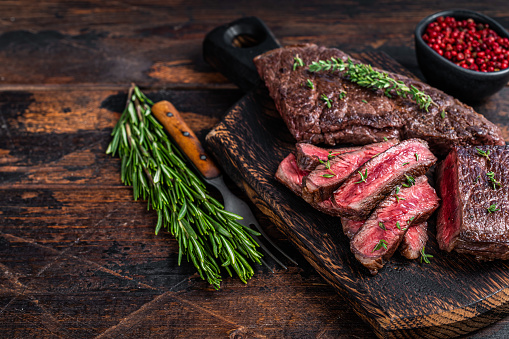 Grilled sliced skirt beef meat steak on a cutting board with herbs. Dark wooden background. Top view. Copy space.