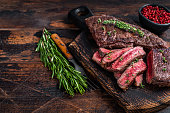 Grilled sliced skirt beef meat steak on a cutting board with herbs. Dark wooden background. Top view. Copy space
