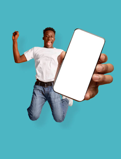 istock Young black man jumping and shouting WOW, going crazy, showing smartphone screen with mockup for new mobile app 1354385459