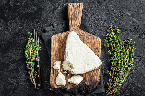Fresh Soft goat cheese on a cutting board with thyme. Black background. Top view.