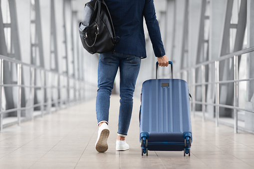 Hombre irreconocible con bolso y maleta caminando en el aeropuerto, vista trasera photo