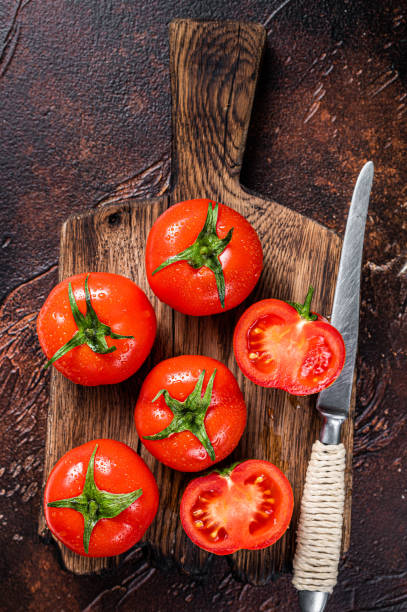 istock Cut Red cherry tomatoes on wooden cutting  board. Dark background. Top view 1354385712