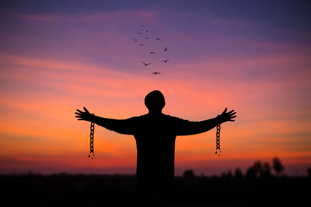 silhouette du jeune homme debout seul avec un beau ciel au coucher du soleil ouvrir les deux bras avec des chaînes sur les bras. il se sentait libéré des chaînes attachées à ses bras. - freedom photos et images de collection