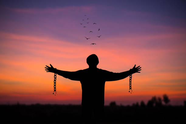 Silhouette of young man standing alone  with beautiful sky at sunset open both arms with chains on his arms. He felt free from the shackles tied to his arms. stock photo