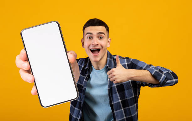 istock Positive millennial man showing smartphone and thumb up, mockup 1354385904
