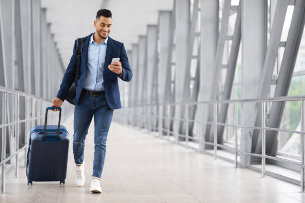 istock Online Check In. Handsome Arab Man Walking In Airport And Using Smartphone 1354386495