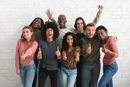 Beautiful multiethnic young people men and women in casual posing together over white brick wall, showing positive emotions, gesturing, smiling, laughing, millennials lifestyle concept