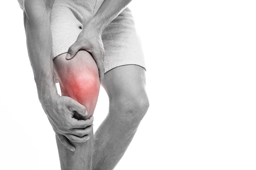 Cropped young european man suffering from knee pain, presses hand to sore spot, highlighted in red, monochrome, isolated on white background. Inflammation, arthritis, trauma, health problem and injury