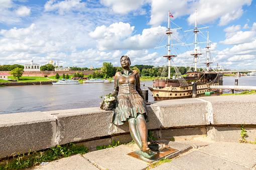 Veliky Novgorod, Russia - August 23, 2019: Sculpture of tired tourist girl on the background of the river and the Kremlin. Girl-Tourist Monument in sunny day