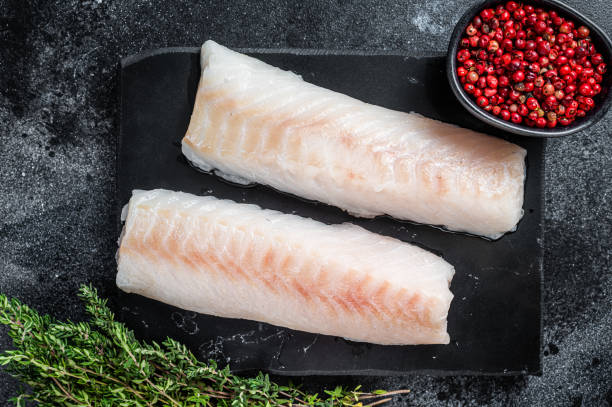 istock Raw cod loin fillet fish on marble board. Black background. Top view 1354388675