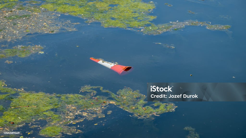 An orange traffic cone floating in a eutrophic river water after being thrown in River Stock Photo