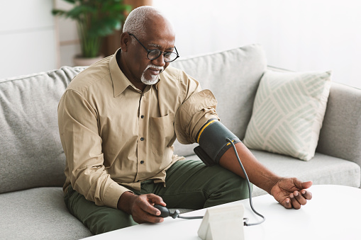 Hombre africano mayor que mide la presión arterial con hipertensión en interiores photo