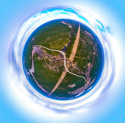 Aerial view of agricultural fields of yellow color crop under a clear blue sky with clouds on sunny warm spring day before sowing. Panorama 360 degrees. Little planet crossed by road. Farming.