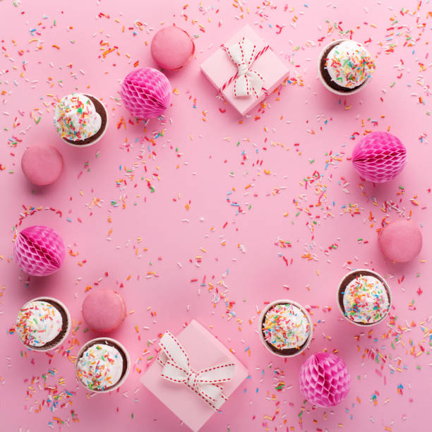 istock Pink paper decorations, sweet macaroons and cupcakes on pink sprinkles background. 1354401449