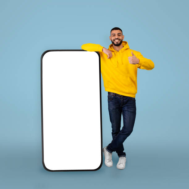istock Mobile offer. Happy arab man leaning on big smartphone with blank screen and gesturing thumb up, blue background 1354402259