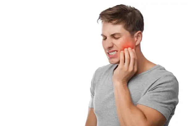 Sad unhappy young handsome caucasian guy suffering from toothache, presses hand to cheek, highlighted in red, isolated on white background, free space. Medicine, health care, teeth and dental problems