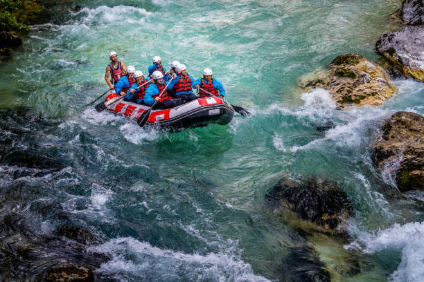 People riding down water in gorge in raft, crystal clear turquoise water making waves around stones stock photo