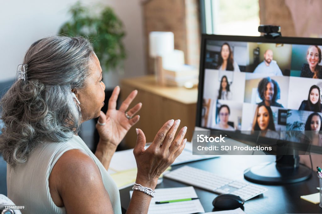 Businesswoman gestures during video call A serious senior businesswoman gestures as she facilitates a staff meeting while working from home. She is talking with her colleagues during a video conference. Video Call Stock Photo
