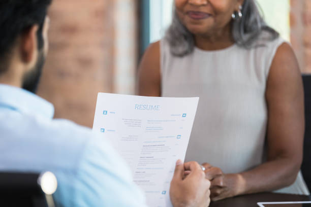 Businessman interviews job candidate A businessman reads a resume during a job interview with a potential employee. good cv stock pictures, royalty-free photos & images