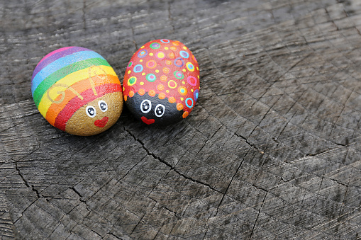 Two hand painted rainbow love bugs on rocks are sitting on a natural wood background.