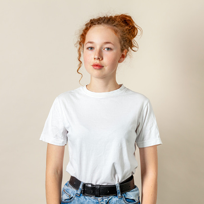 Close-up studio portrait of a 15 year old girl with curly red hair in a white t-shirt on a beige background