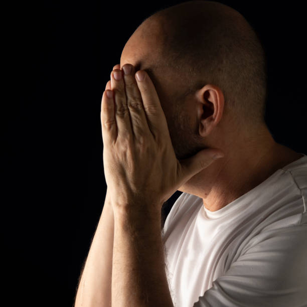 istock Person with hands on face against dark background. 1354412637