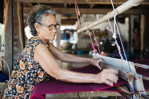 Traditional Isan Thai silk weaving. old woman hand weaving silk in traditional way at manual loom. Kalasin, Thailand.