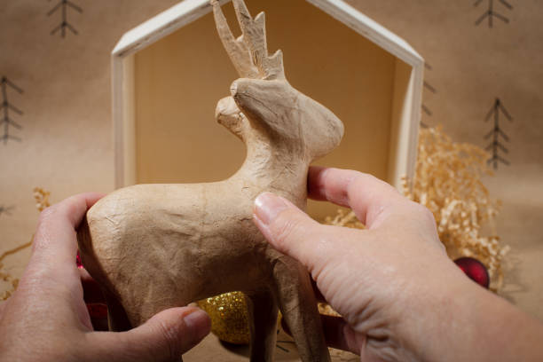 Miniature wooden house shining with warm lights, featuring tiny Christmas tree and reindeer decoration on a light purple background with bokeh