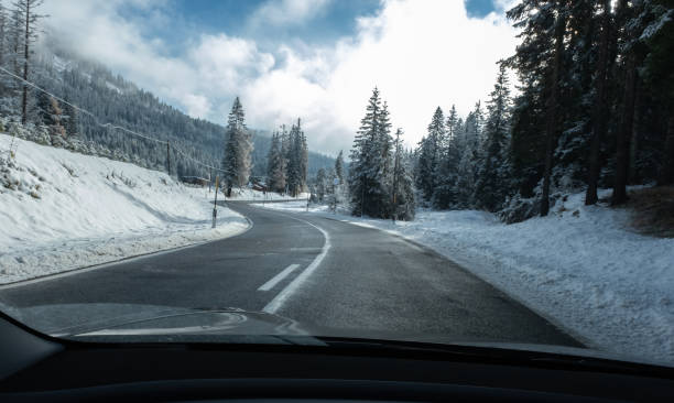 雪に覆われたアルプス山脈を持つ電気自動車のフロントガラスの後ろから移動中のショット。寒い曇りの秋の日。povの一人称は、アスファルト山道で撮影されたビュー。選択的フォーカス - mountain landscape rock european alps ストックフォトと画像