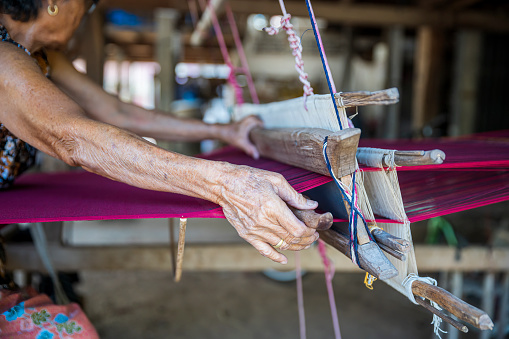 Traditional Isan Thai silk weaving. Hand of an old woman weaving silk in traditional way at manual loom. Kalasin, Thailand.