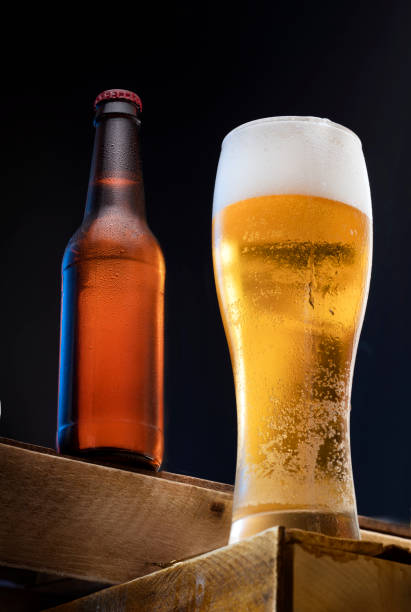 a glass of cold fresh light beer and a bottle of steamed cold beer in the background on a black background. a party or celebration in a beer restaurant stock photo