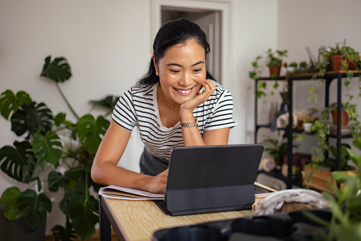 Smiling Asian woman talking with client on online video call meeting while standing in her workshop.