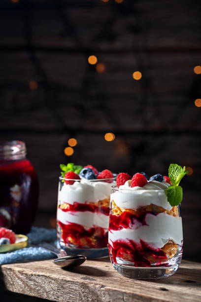 on a wooden background with lights, dessert with cream, cottage cheese, raspberries and blueberries in a glass - treated wood imagens e fotografias de stock