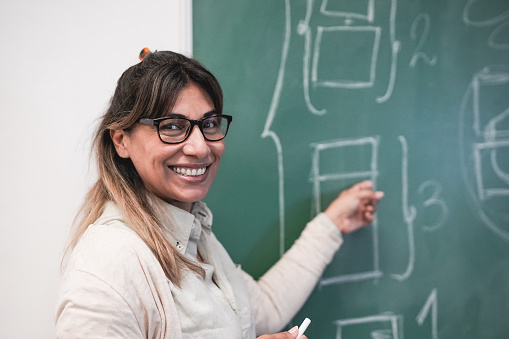 Mature latin female teacher smiling on camera inside classroom - Concept of online class