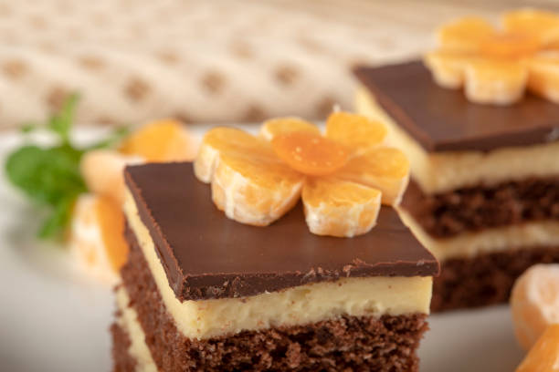 Home made chocolate cake with custard cream decorated with tangerine. The cake is on a plate on the table with a checkered tablecloth. Top of the cake is chocolate icing. It ready to eat.