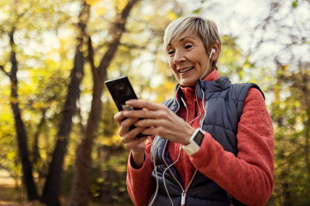 istock Senior woman using smartphone wearing headphones 1354454799
