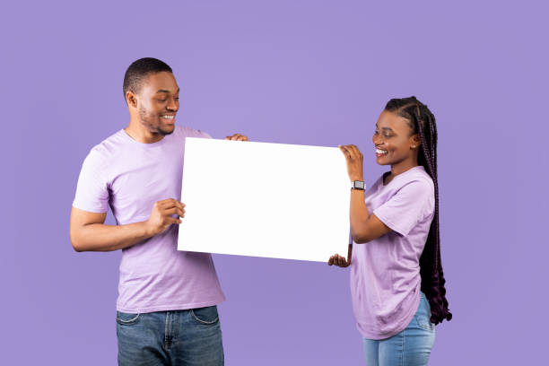 istock Black couple holding and looking at blank white advertising placard 1354464110