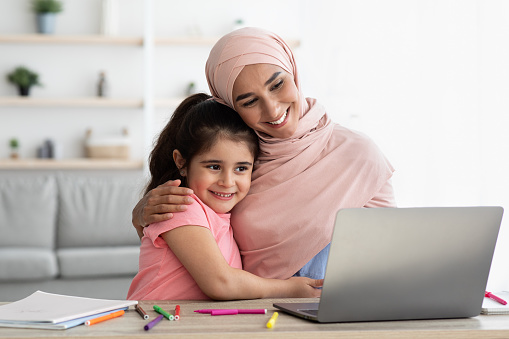 Distance Learning. Islamic Mother In Hijab And Her Cute Little Daughter Using Laptop At Home Together, Portrait Of Young Muslim Lady Helping With Online Homework To Preteen Female Child, Closeup