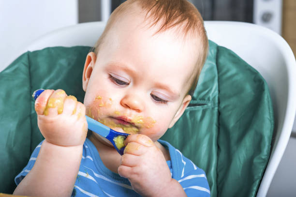 Handsome toddler eating spoon with fruit vegetable puree close-up. Baby complementary feeding, food allergy, intolerance concept.