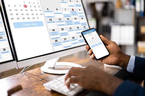 African Man Organizing Appointment Schedule Using Cellphone And Calendar