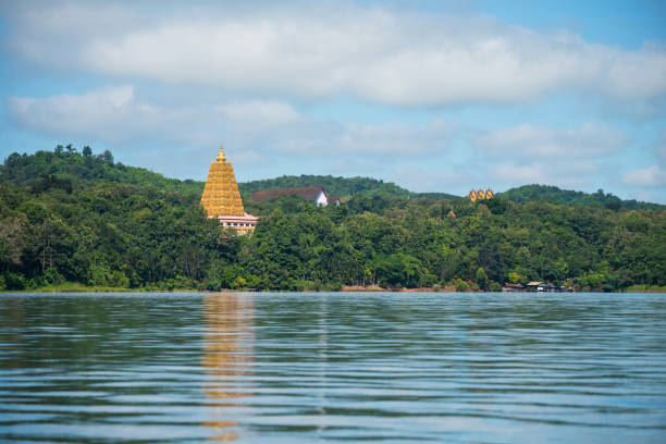 Bodhgaya gold pagoda and Wang Wiwekaram temple with tree forest against blue sky by river in Sangkhlaburi, Kanchanaburi, Thailand. Famous travel destination captured by boat, Siam.