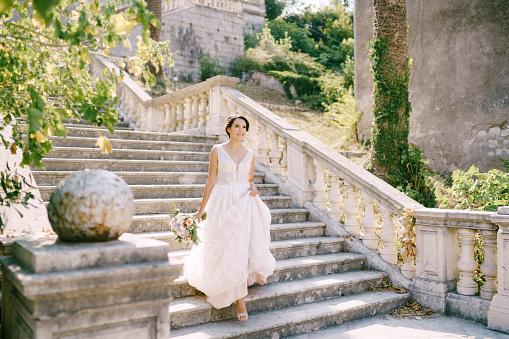 The bride in wreath descends the picturesque stairs of the ancient temple in Prcanj, back view . High quality photo