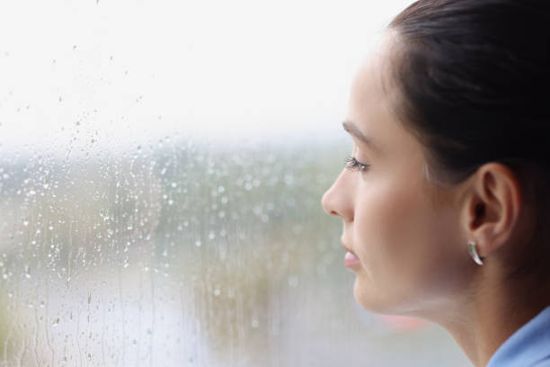 istock Young pensive woman looking out window at rain 1354514646