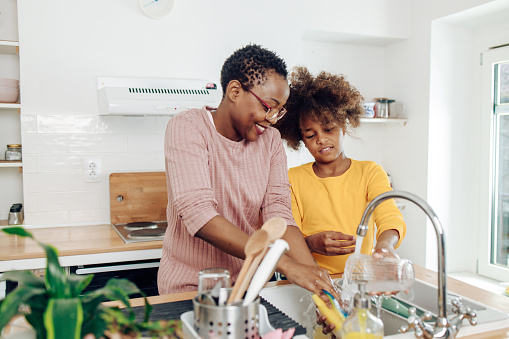 African American teenage girl helping her grandmother with washing dishes.
