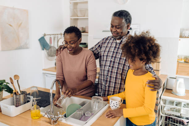 african american senior woman washing dishes and enjoying with granddaughter and husband - senior getting groomed studio imagens e fotografias de stock