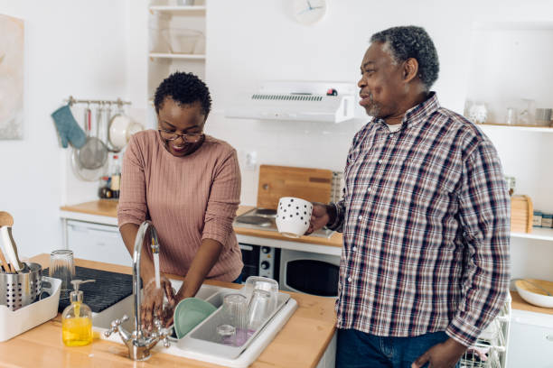 african american senior man enjoying coffee while his wife washing dishes - senior getting groomed studio imagens e fotografias de stock
