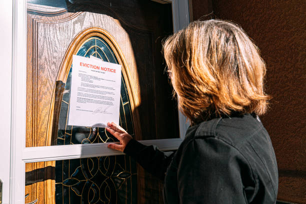 Middle-Age Woman Reaching and Removing an Eviction Notice Taped on the Front Door of a Home in a Residential Suburban Neighborhood stock photo
