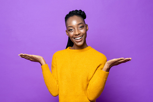 Smiling young African American woman opening hands to empty space in isolated purple studio background