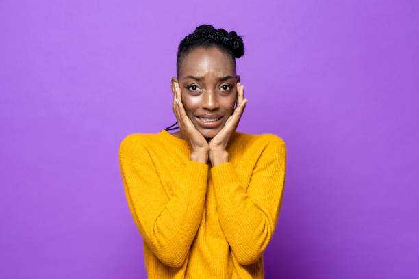 young african-american woman feeling fear and frightened with hands on cheeks in purple isolated studio background - offense imagens e fotografias de stock