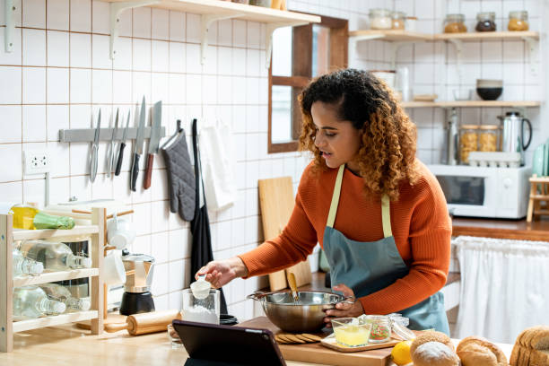 istock Young beautiful African American woman in kitchen learning online virtual cooking class from tablet computer at home 1354524853